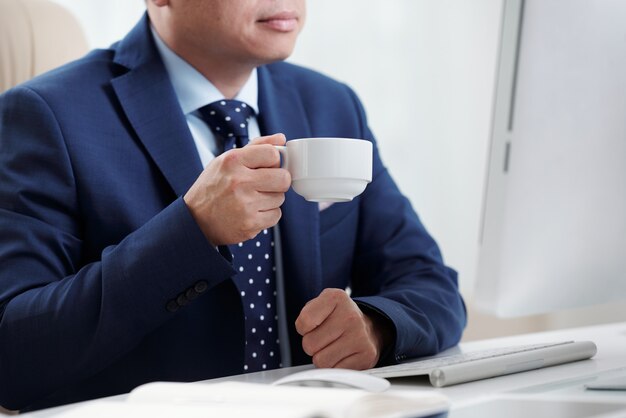 Uomo d'affari potato che mangia caffè alla sua scrivania che esamina lo schermo del computer