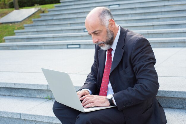 Uomo d'affari premuroso che per mezzo del computer portatile mentre sedendosi sulle scale