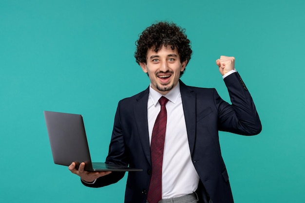 Uomo d'affari riccio carino bel ragazzo in abito nero e cravatta rossa in possesso di un computer portatile ed eccitato