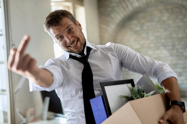 Uomo d'affari scontento che mostra il dito medio verso la telecamera dopo aver perso il lavoro in ufficio