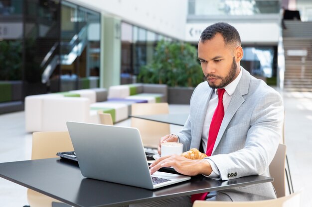 Uomo d'affari serio che utilizza computer portatile nel caffè