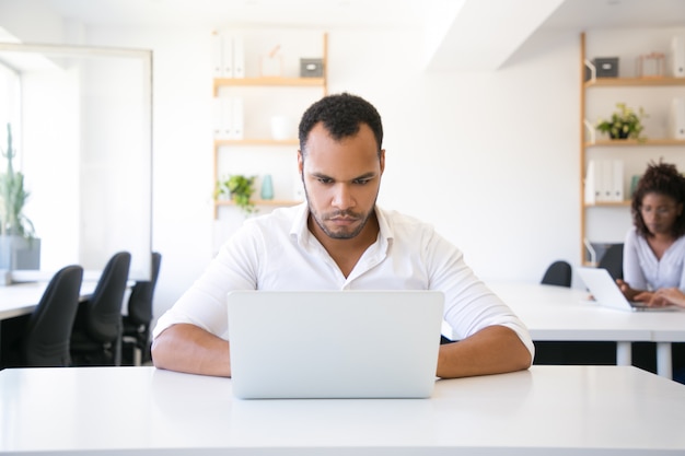 Uomo d'affari sicuro serio che utilizza computer portatile nell'ufficio