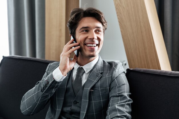 Uomo d'affari sorridente bello in vestito che parla sul telefono cellulare