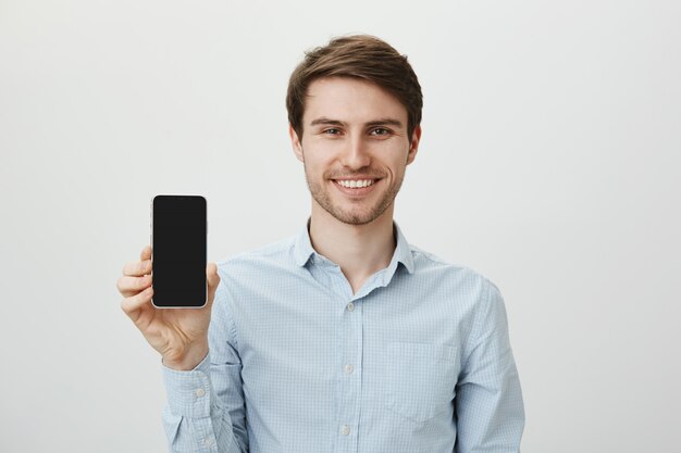 Uomo d'affari sorridente bello promuovere l'applicazione mobile, mostrando il display dello smartphone
