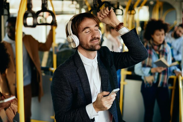 Uomo d'affari sorridente che ascolta musica con gli occhi chiusi mentre si sposta con i mezzi pubblici