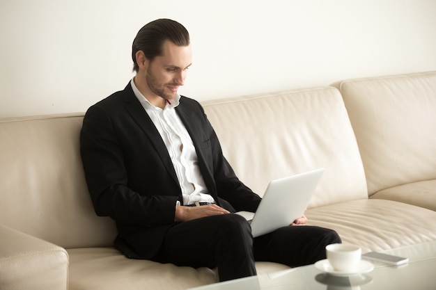 Uomo d&#39;affari sorridente che lavora a distanza a distanza dal computer portatile da casa.