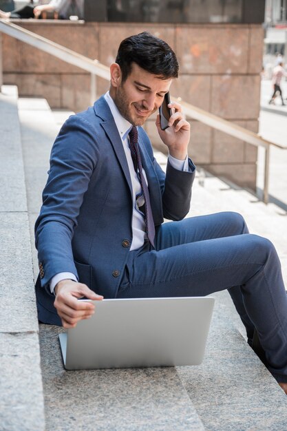 Uomo d&#39;affari sorridente che parla sul telefono e sul computer portatile di lettura rapida