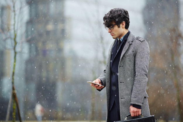 Uomo d'affari Using Smartphone in Snowy Street