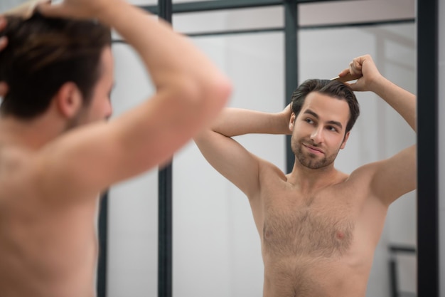 Uomo dai capelli scuri che si spazzola i capelli allo specchio