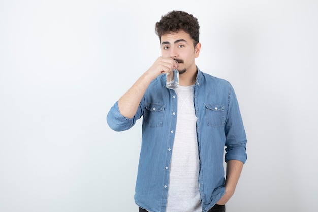 uomo dall'aspetto serio che beve bicchiere d'acqua su bianco.