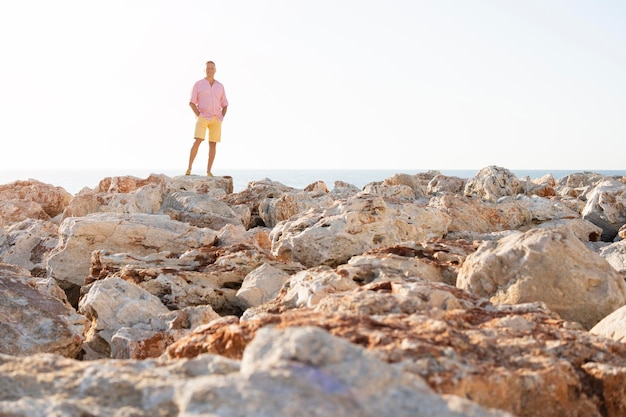 Uomo del colpo lungo che posa sulle rocce