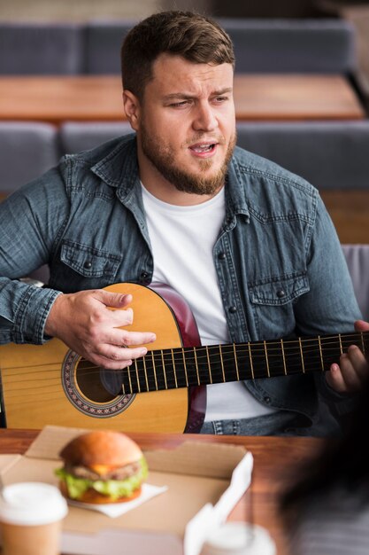 Uomo del colpo medio che gioca chitarra al tavolo