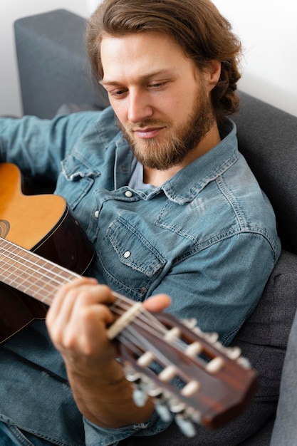 Uomo del colpo medio che suona la chitarra a casa