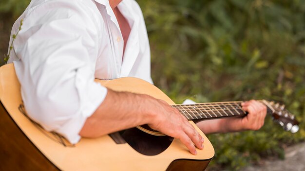 Uomo del colpo medio che suona la chitarra nella natura