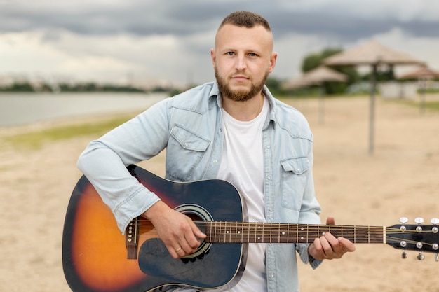 Uomo del colpo medio che suona la chitarra su una spiaggia