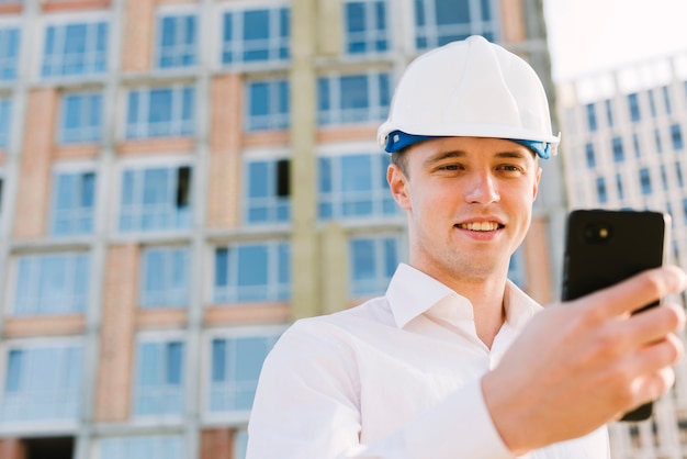 Uomo del colpo medio con il casco che esamina telefono