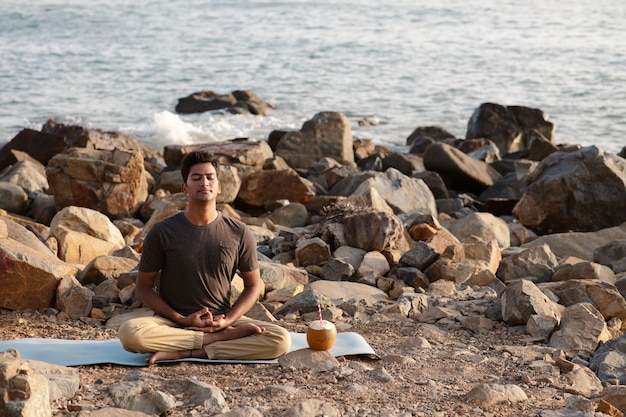 Uomo del colpo pieno che fa yoga sulla stuoia in natura