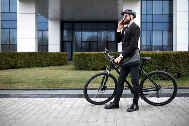 Uomo del colpo pieno con la bicicletta che parla al telefono