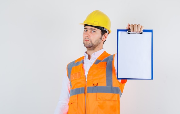 Uomo del costruttore che tiene appunti in camicia, uniforme e che sembra serio, vista frontale.