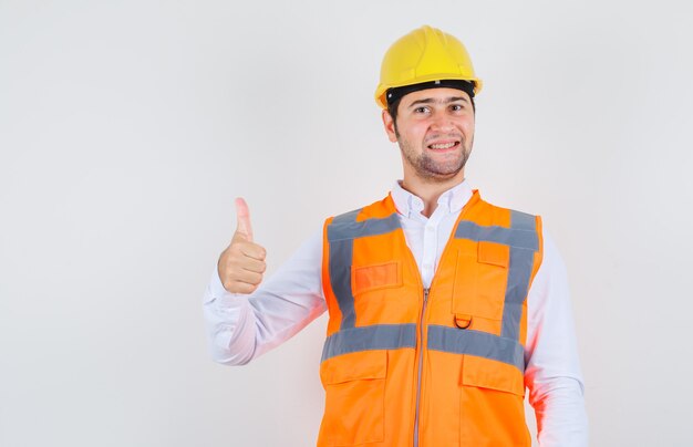 Uomo del costruttore in camicia, uniforme che mostra pollice in su e che sembra allegro, vista frontale.