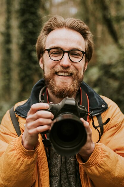 Uomo del fotografo che sorride mentre tiene la macchina fotografica nel bosco