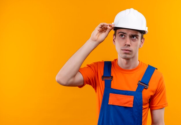Uomo del giovane costruttore che indossa l'uniforme della costruzione e il pensiero del casco di sicurezza