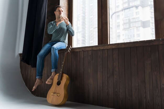 Uomo del musicista in casa suonando il flauto vista bassa