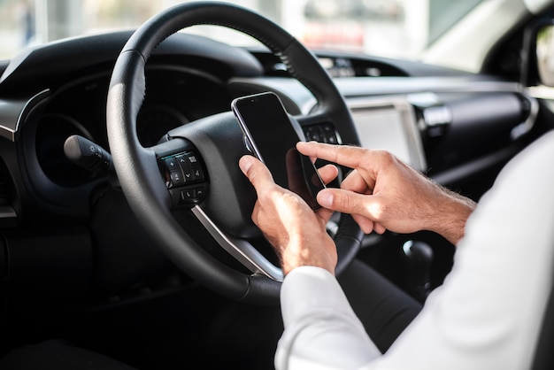 Uomo del primo piano al volante che controlla telefono