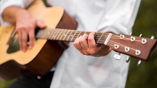 Uomo del primo piano che gioca la chitarra nella natura