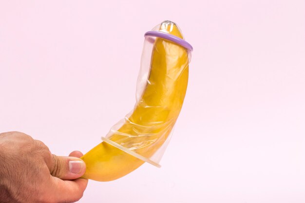Uomo del primo piano che tiene una banana con il preservativo