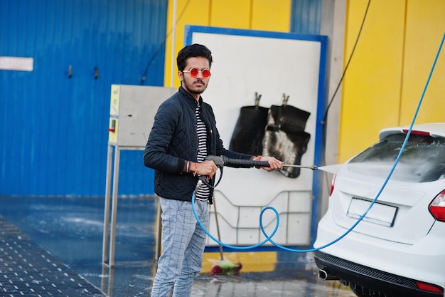 Uomo del sud asiatico o maschio indiano che lava il suo trasporto bianco sull'autolavaggio