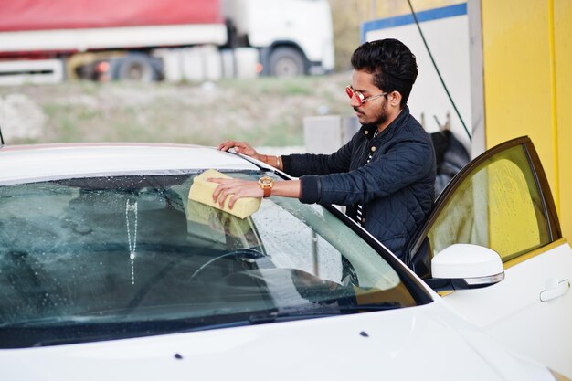 Uomo del sud asiatico o maschio indiano che lava il suo trasporto bianco sull'autolavaggio