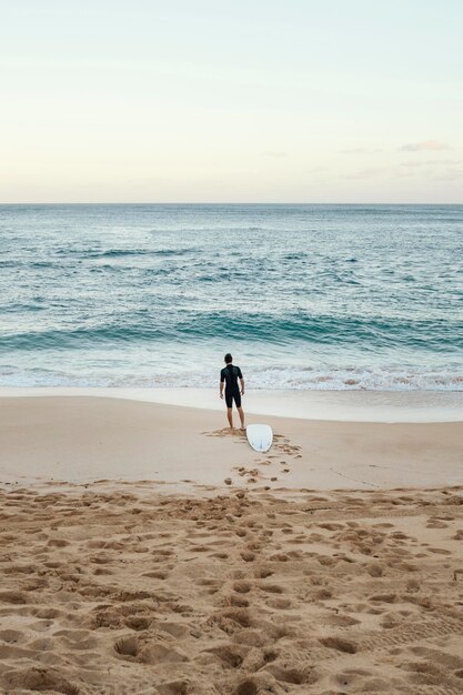 Uomo del surfista che esamina il colpo lungo verticale del mare