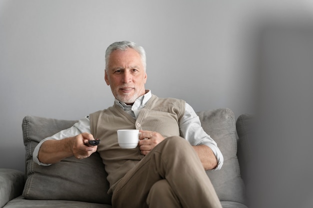 Uomo del tiro medio che tiene tazza sul divano