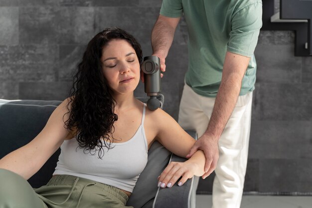 Uomo dell'angolo alto che usa la pistola di massaggio sulla donna