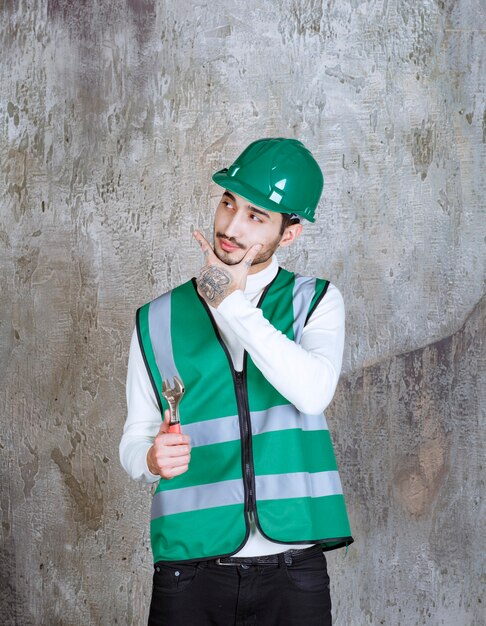 Uomo dell'ingegnere in uniforme gialla e casco che tiene una chiave metallica per la riparazione e sembra premuroso.