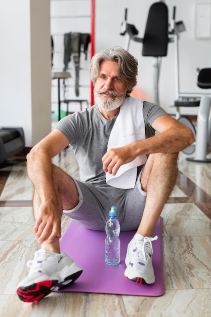 Uomo della foto a figura intera che si siede sulla stuoia di yoga
