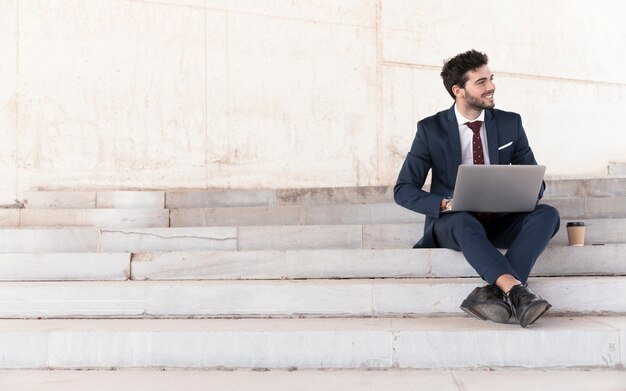 Uomo della foto a figura intera sulle scale che lavorano al computer portatile