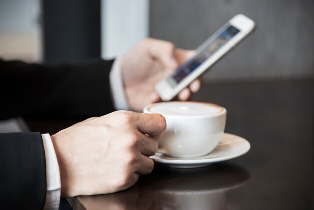 Uomo di affari che utilizza telefono cellulare mentre bevendo caffè in caffetteria