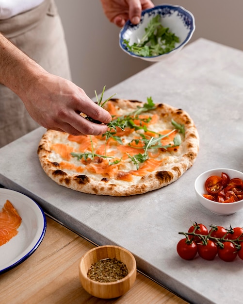 Uomo di alto angolo mettendo la rucola sulla pasta per pizza al forno con fette di salmone affumicato