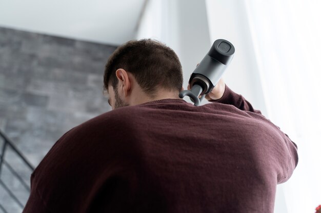 Uomo di angolo basso che usa la pistola di massaggio