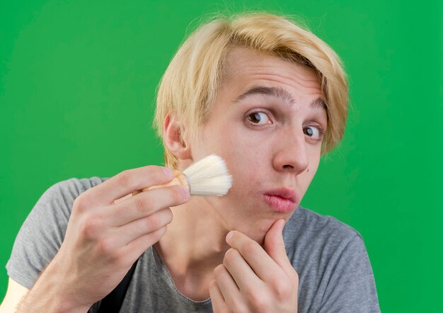 Uomo di barbiere professionista in grembiule che tiene pennello da barba toccando il suo viso con esso