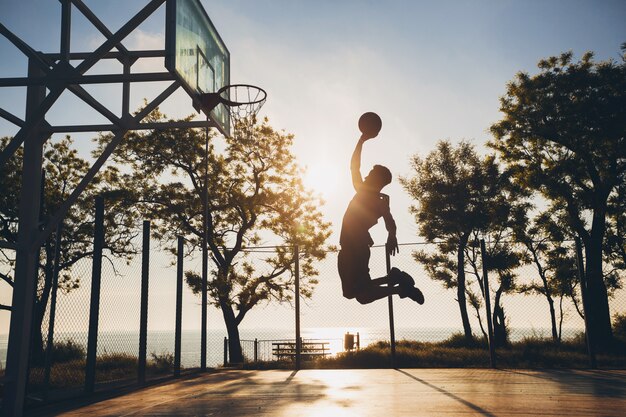 Uomo di colore che fa sport, gioca a basket all'alba, salta la sagoma