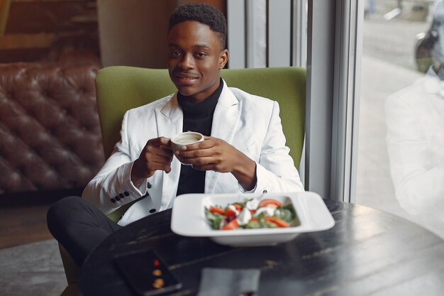 Uomo di colore che si siede in un caffè e che mangia un'insalata di verdure