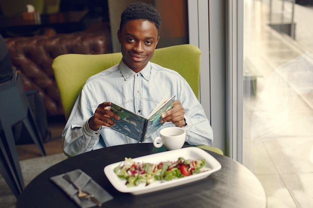 Uomo di colore che si siede in un caffè e che mangia un'insalata di verdure