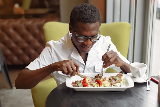 Uomo di colore che si siede in un caffè e che mangia un'insalata di verdure