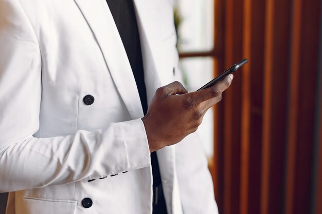 Uomo di colore in una giacca bianca in piedi con un telefono