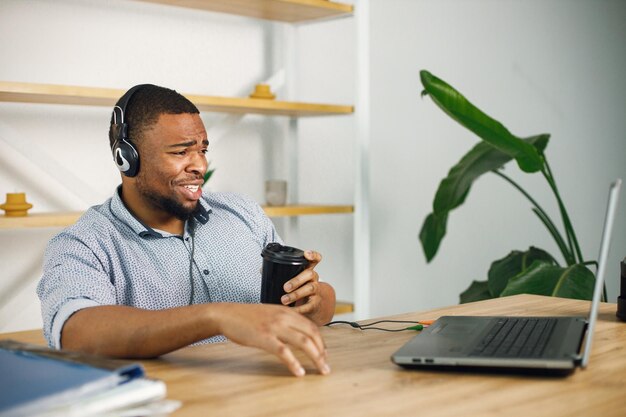 Uomo di colore seduto in ufficio che indossa un auricolare ed effettua una videochiamata