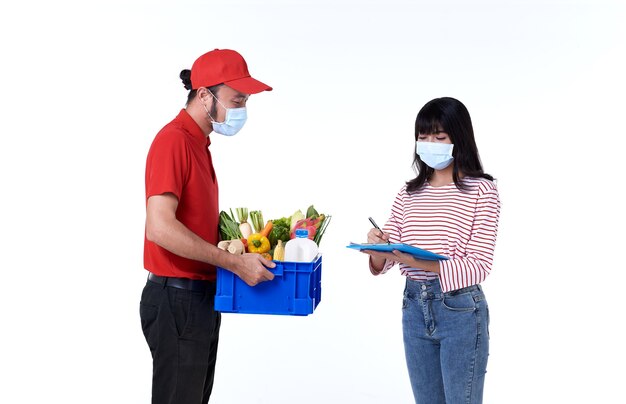 Uomo di consegna asiatico che indossa la maschera per il viso in uniforme rossa con scatola di generi alimentari di cibo