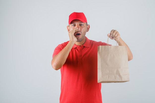 Uomo di consegna che tiene il sacchetto di carta e che gesturing nella vista frontale uniforme rossa.